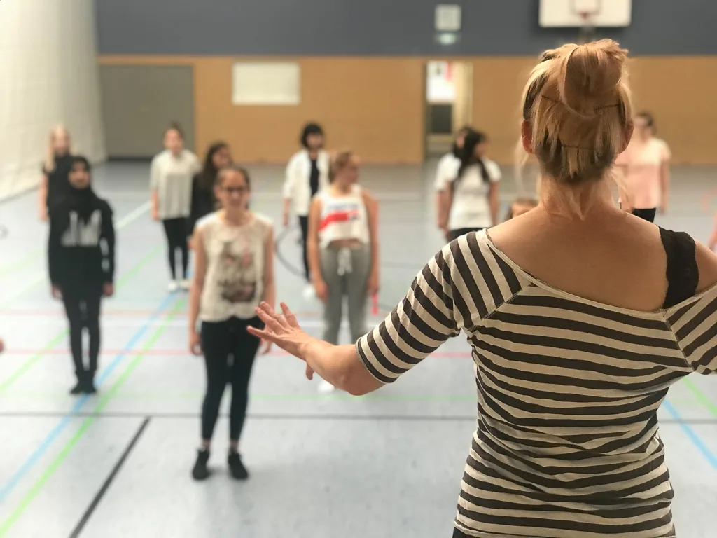 Person leitet die Tanzprobe in der Sporthalle an.